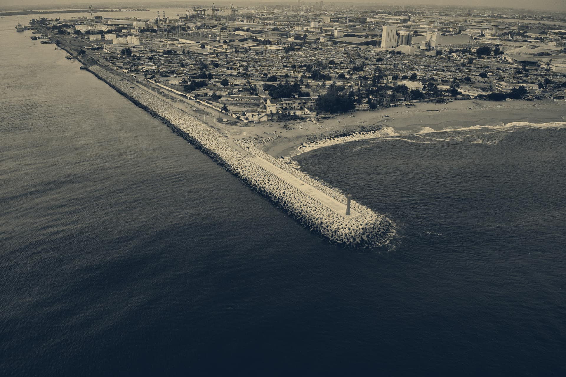 Vue aérienne de la côte d'Abidjan, une digue avancée dans l'océan et la ville derrière.